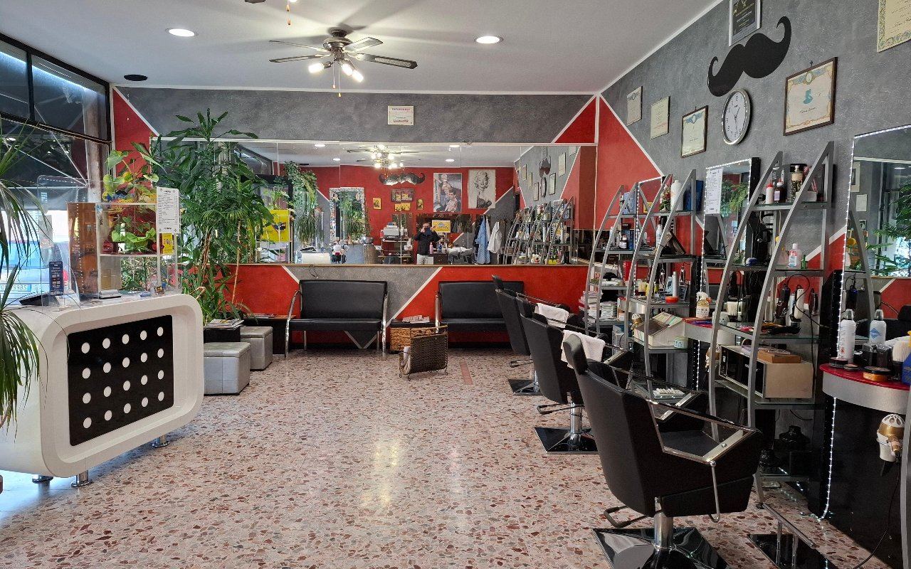 Interno del barber shop: poltrone nere, specchi, pareti rosse e grigie e pavimento in graniglia